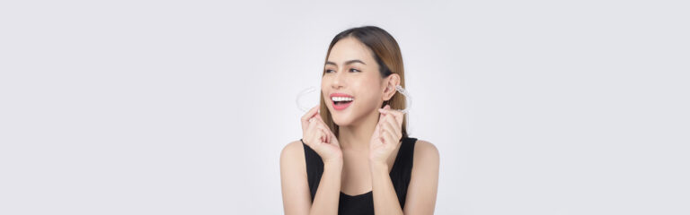 A smiling lady holding Invisalign clear aligners in hand